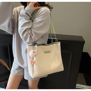 Detail of minimalist beige tote bag with green trim and plush eye pendant on model