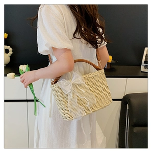 Detailed texture of beige woven straw bag featuring white lace bow and pearl chain handle