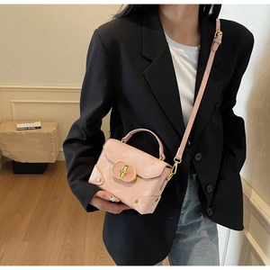 Pink matte leather box handbag with gold metal clasp carried by a model in a blazer
