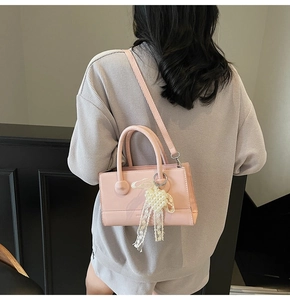 Detailed view of pink crossbody bag with lace bow and pearl charm on a model