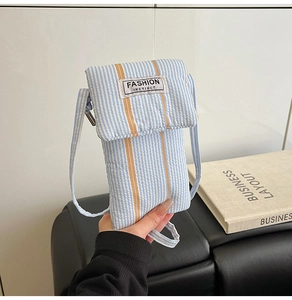 Detail of blue striped fabric crossbody phone bag with orange accents and fashion patch