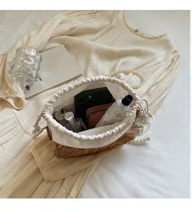Detail of straw woven bag showing interior capacity with phone, perfume and pearl strap