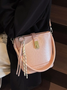Sac seau rose texture litchi avec fermoir doré et breloque tressée porté par un modèle