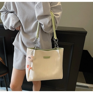 Detail of cream tote bag with light green straps and cute pink plush monster charm