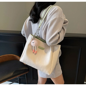 Detail of cream tote bag featuring wavy texture, green straps, and pink plush charm