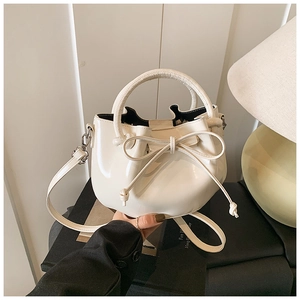 Detail of cream oil-wax leather bucket bag with decorative bow and round top handle