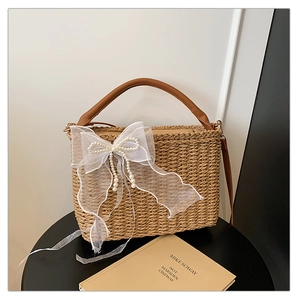 Detail of straw woven handbag with large white organza bow and pearl accents