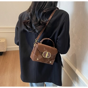 Detailed view of brown glossy box bag with gold oval lock and metallic rivets worn by model