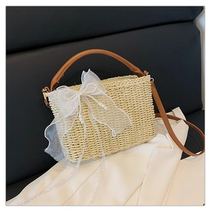 Detail of woven straw bag featuring a large white lace bow and elegant pearl accents