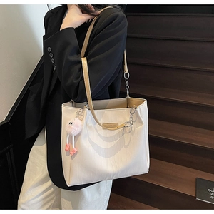 Detailed view of creamy white textured tote bag with pink plush charm on wooden stairs