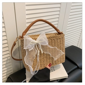 Detail of straw woven handbag with white lace bow, pearls and brown leather strap