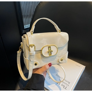 Detail of cream white handbag featuring a gold oval clasp and textured leather handgrip