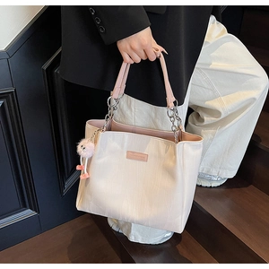 Detail of beige tote bag featuring pink chain straps and fuzzy plush pendant on stairs