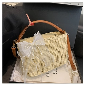 Detail of straw handbag with white lace bow, pearl charms and leather straps in a gift box