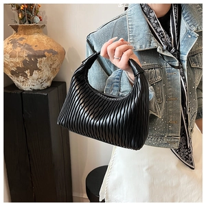 Detailed view of black pleated dumpling bag with textured leather and thick top handle
