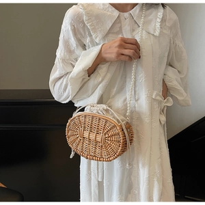 Detail of hand-woven straw shoulder bag with elegant faux pearl strap and drawstring liner