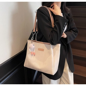 Detail of off-white tote bag with pink straps and plush charm on a model's shoulder