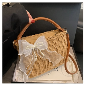 Detail of straw woven handbag with large lace bow, pearls, and leather handles in a gift box