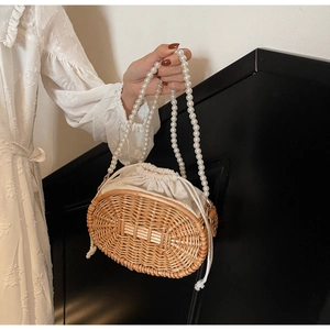 Detail view of woven rattan bucket bag with elegant long pearl beaded handle and inner pouch