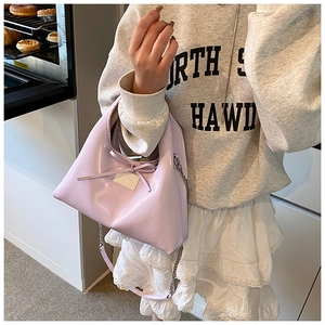 Detailed view of lavender faux leather dumpling bag with decorative bow and chain strap