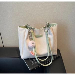 Close-up of beige tote bag with light green straps and pink plush pendant on a book