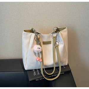 Detail of off-white tote bag with bark texture, green handle and plush pendant
