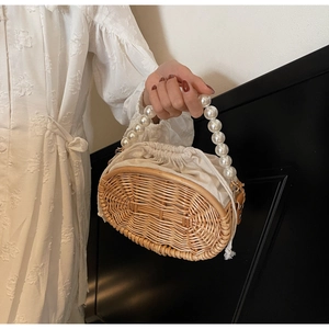 Detail view of woven straw bag with white faux pearl handle and canvas drawstring lining