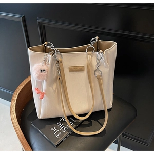 Close-up of cream leather tote bag with brown handles, chain strap and plush pendant