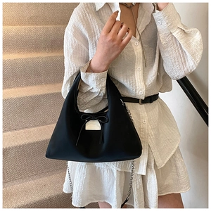 Detail of minimalist black dumplings bag with bow decoration and silver chain strap