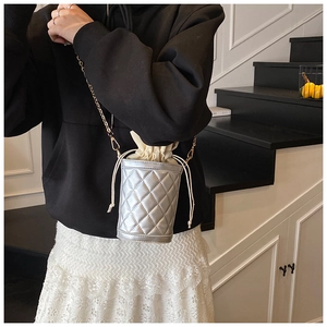 Detail of silver quilted bucket bag featuring a gold chain and drawstring inner pouch