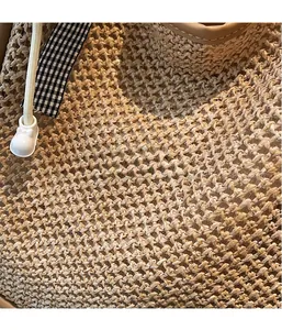 Détail de la texture d'un sac en paille tissée avec sangle à carreaux et breloque