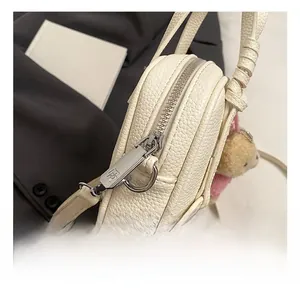 Detail shot of beige lychee texture mini bag with silver zipper and cute teddy bear charm