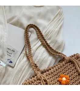 Detail of hand-woven straw tote bag with orange floral patterns and thick braided straps