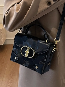 Elegant black glossy box handbag with gold metal clasp carried by a model in a khaki coat