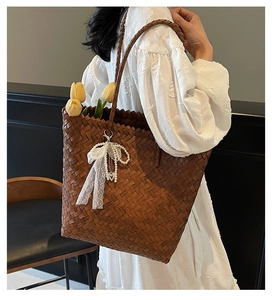 Détail du sac cabas en paille avec nœud en dentelle et perles sur une robe blanche