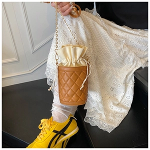 Detail of brown quilted bucket bag with cream drawstring and gold chain shoulder strap