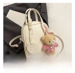 Close-up of white pebble leather crossbody bag with a cute bear and smiley charm