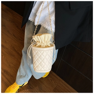 Close-up of beige quilted bucket bag featuring a drawstring closure and gold chain strap