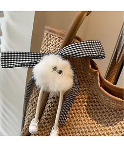 Gros plan d'un porte-clés en peluche blanche avec nœud sur un sac fourre-tout en paille