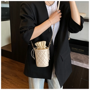 Close-up of a white quilted bucket bag with gold chain strap worn by a female model