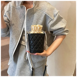 Detail of black quilted bucket bag featuring a cream drawstring closure and gold chain
