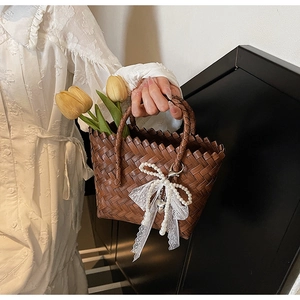 Détail d'un sac panier en paille avec nœud en dentelle et perles porté par un mannequin