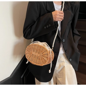 Detail of straw woven bag with elegant pearl strap and white drawstring lining on a model