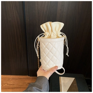 Detail of cream quilted bucket bag featuring drawstring closure and gold chain strap