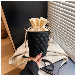 Detail of black quilted bucket bag featuring a beige drawstring pouch and gold chain strap