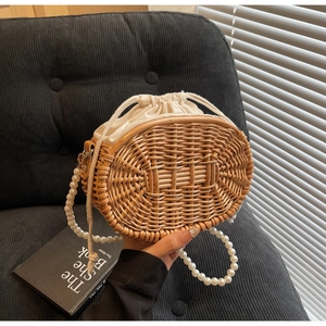 Detailed view of woven rattan bag with faux pearl strap and drawstring liner bag