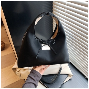 Detail of black trapezoid dumpling bag with bow decoration and metal chain strap