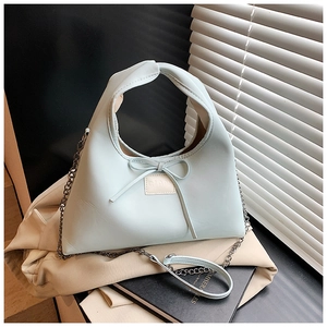 Close-up of mint green leather dumpling bag with decorative bow and metal chain strap