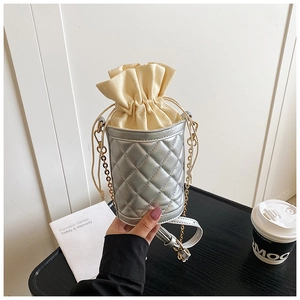 Detail of silver quilted bucket bag with cream drawstring closure and metal chain strap