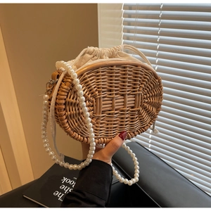 Detail of hand-woven straw bucket bag with large pearl strap and canvas drawstring liner
